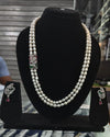 Pearl necklace with diamond and gemstone clasp on a black stand, with matching earrings.