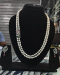 Pearl necklace with diamond and gemstone clasp on a black stand, with matching earrings.