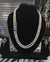 Pearl necklace with diamond and gemstone clasp on a black stand, with matching earrings.