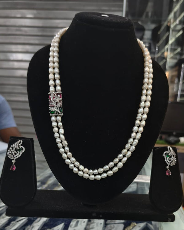 Pearl necklace with diamond and gemstone clasp on a black stand, with matching earrings.